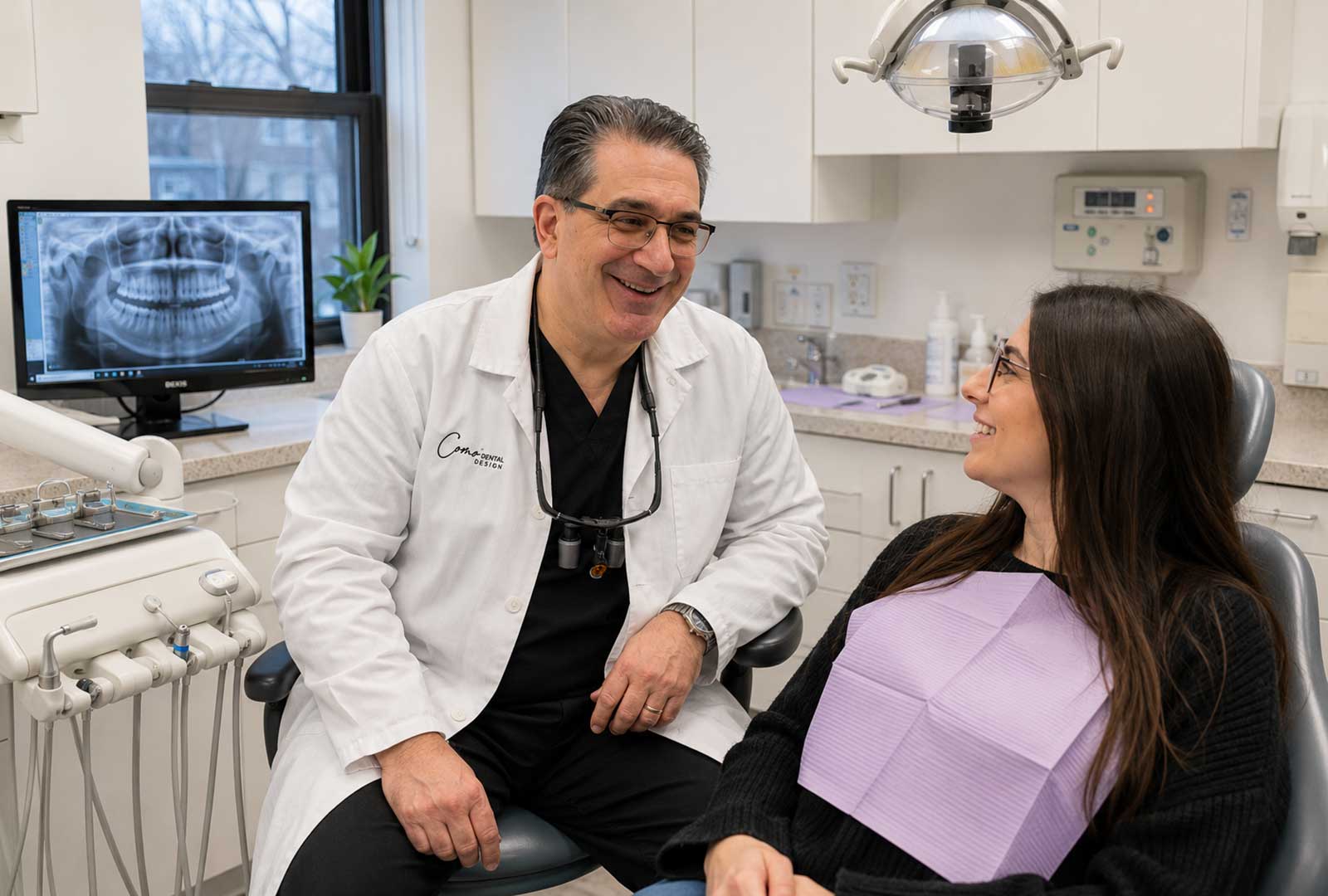 Dr. John Como consulting with a patient in a modern dental treatment room, reviewing digital imaging and discussing personalized dental care in a state-of-the-art New Rochelle practice.