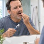 Man checking his gums in the mirror after noticing slight bleeding while brushing.